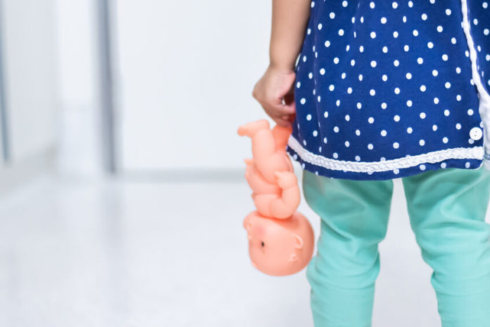 Petite fille de dos tenant une poupée dans la main