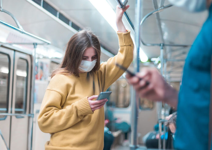 Jeune femme avec masque dans le métro regardant son smartphone
