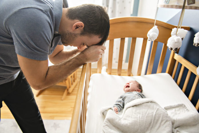 Père épuisé au-dessus du lit de son bébé